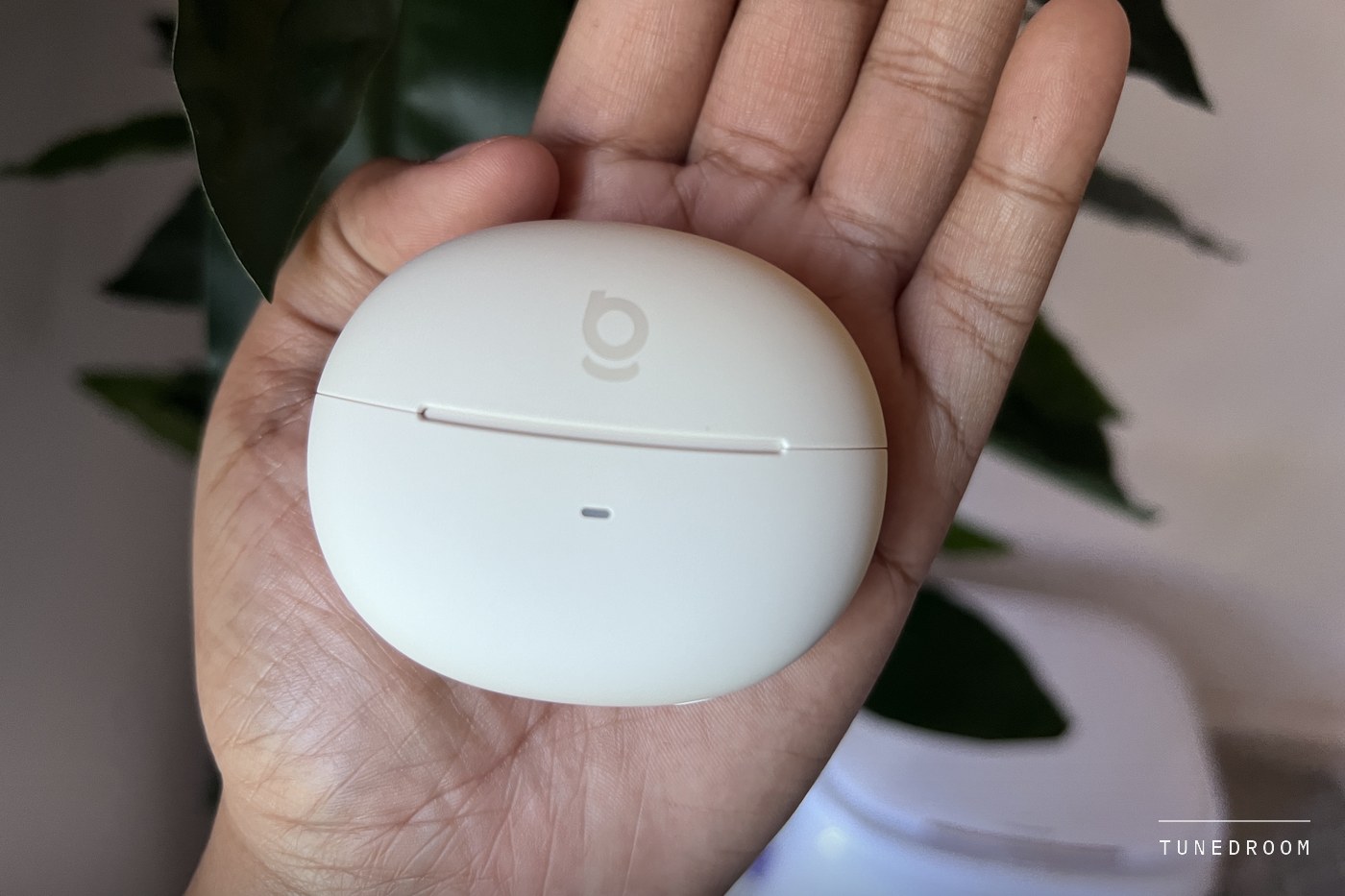 The closed cream charging case of the Bowie MC2 resting in an open palm