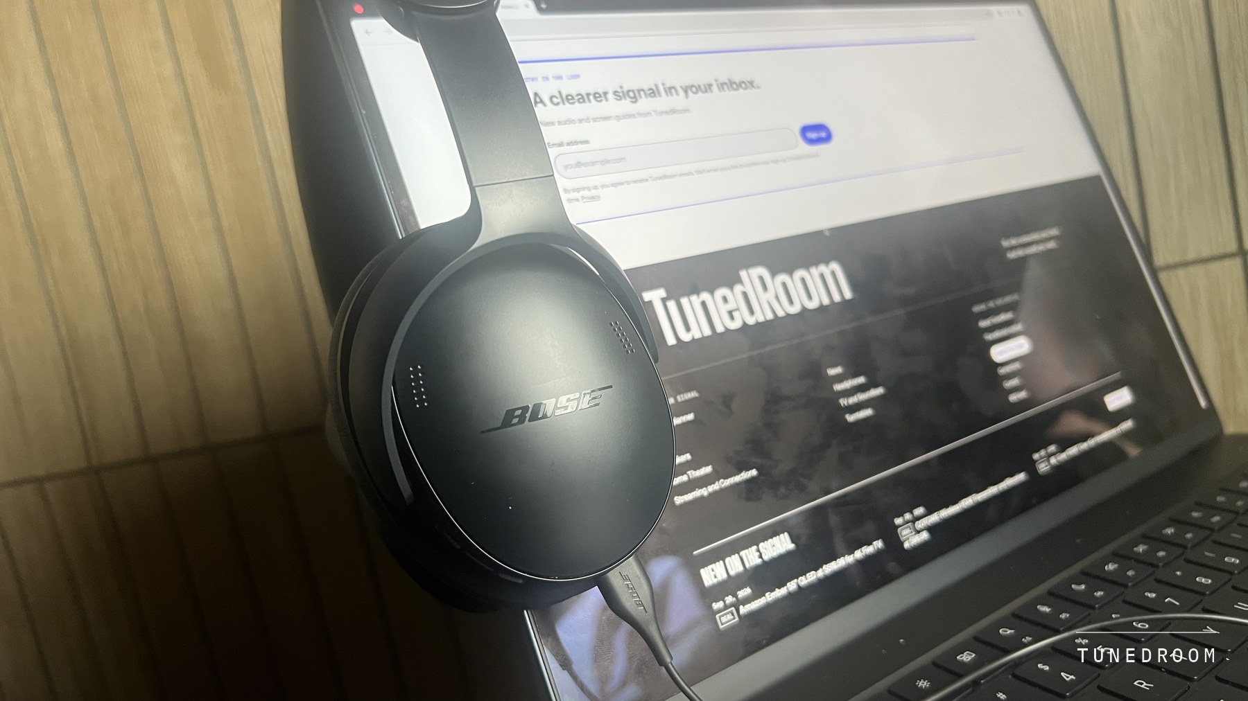 The QuietComfort Headphones resting against an open laptop with the USB-C cable running from the earcup down to the machine