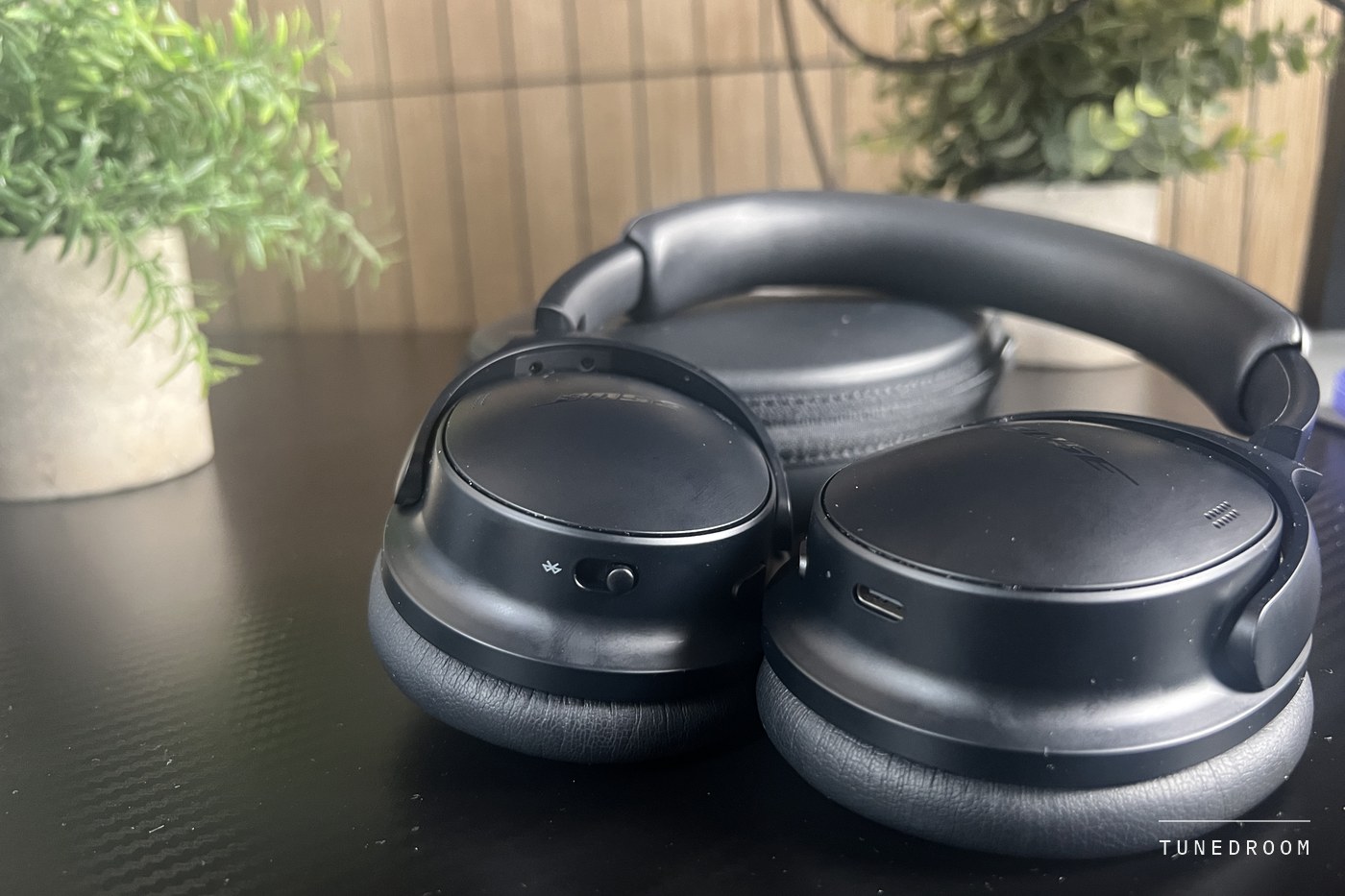 The headphones folded flat on a dark desk beside a plant