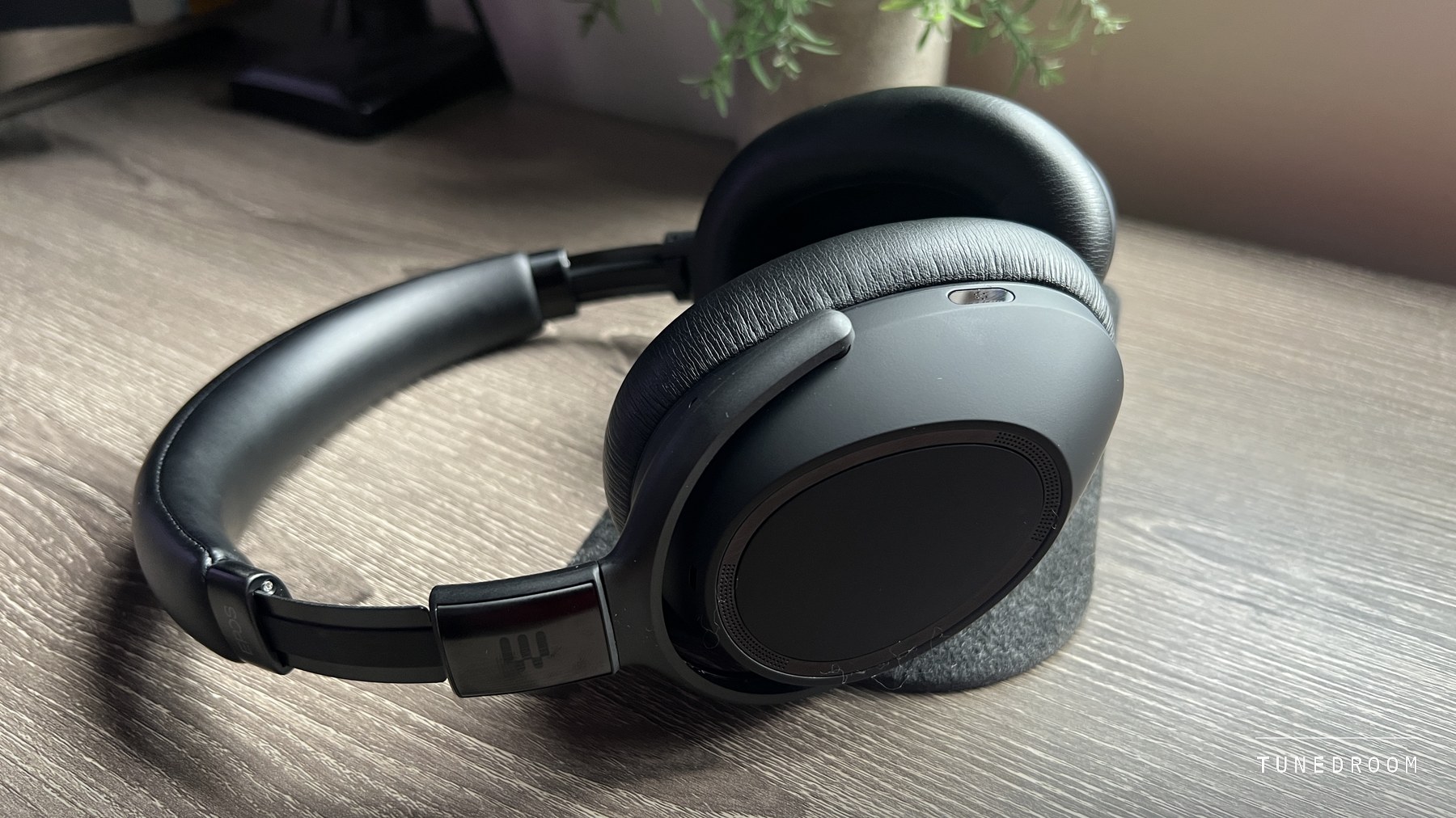 The EPOS Adapt 660 lying on its side on a grey felt pad on a wooden desk, its matte black earcup and headband in profile