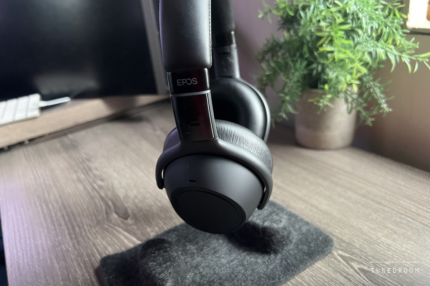 One closed earcup of the Adapt 660 hanging from its headband above a felt pad, the EPOS logo on the slider