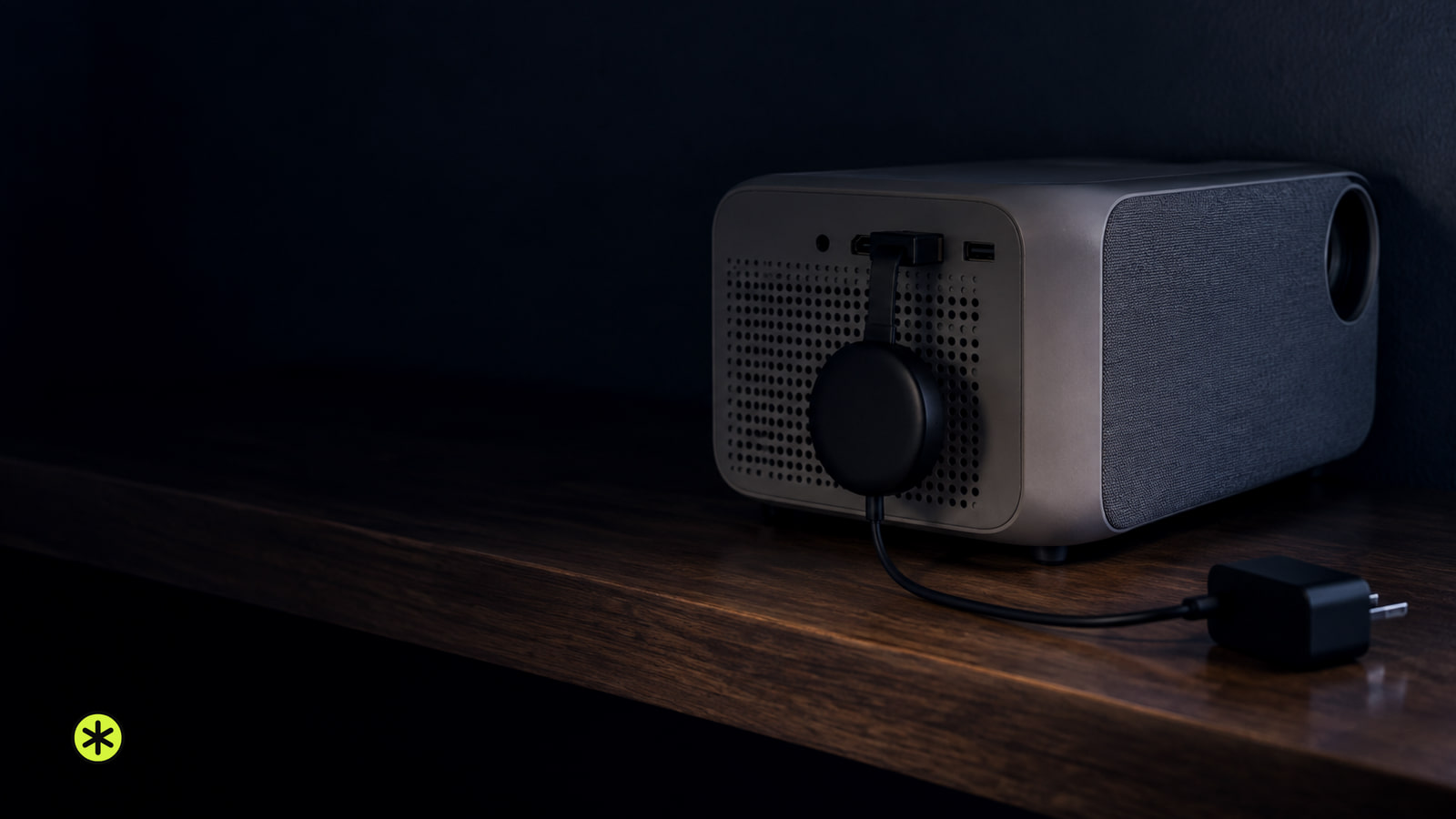 Grey projector on a walnut shelf seen from behind, a small black streaming dongle plugged into its rear port, lit by a cool glow at night.