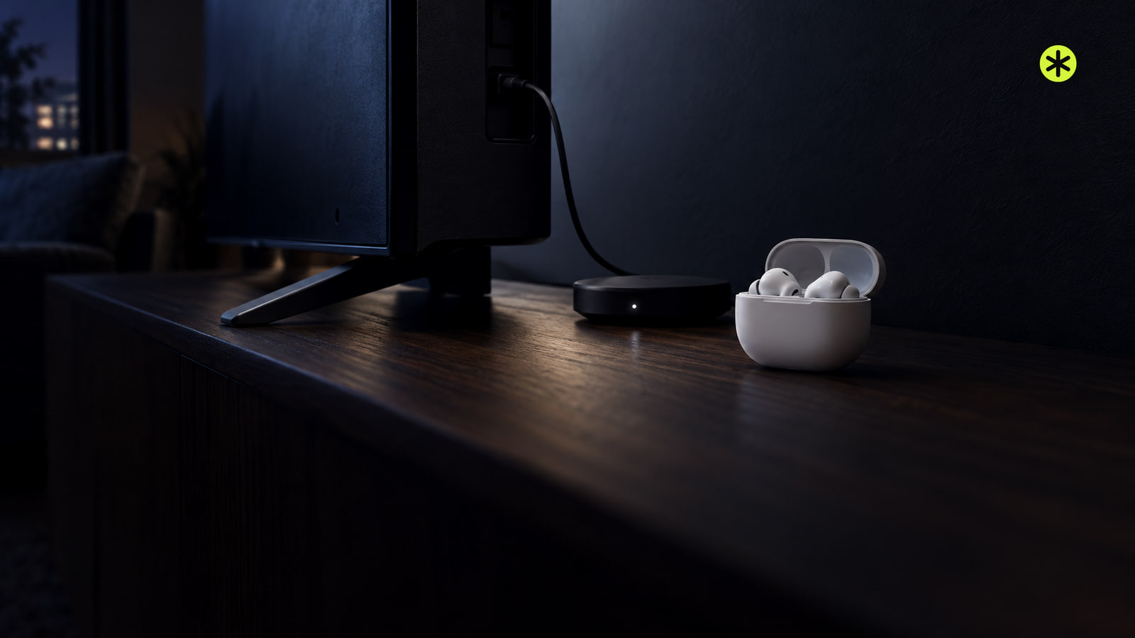 White earbuds in an open case beside a small black transmitter cabled to the back of a TV on a walnut console, in cool screen light.