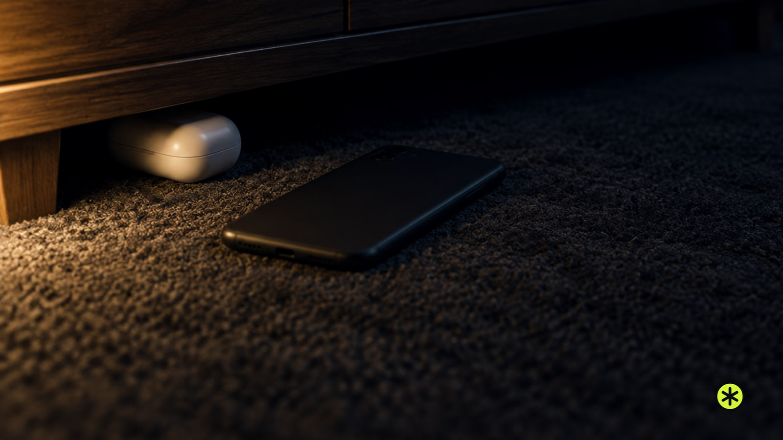 White earbud case lying closed on a charcoal rug half under a walnut console, a phone face down beside it, lit low by one warm lamp.