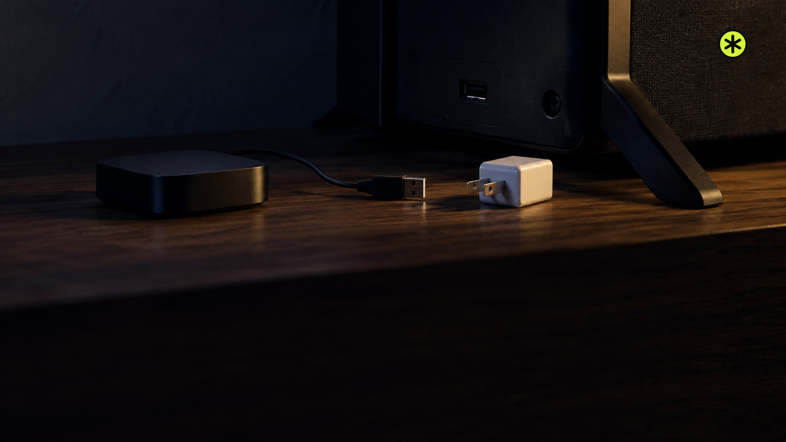 Small black streaming player on a walnut console behind a dark TV, its USB cable unplugged beside a white wall adapter, lit by a low warm lamp.
