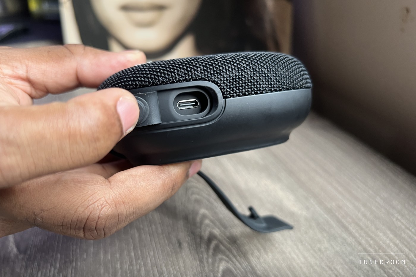 A hand holding the Micro 3 with the rubber cover pulled back from its USB-C charging port