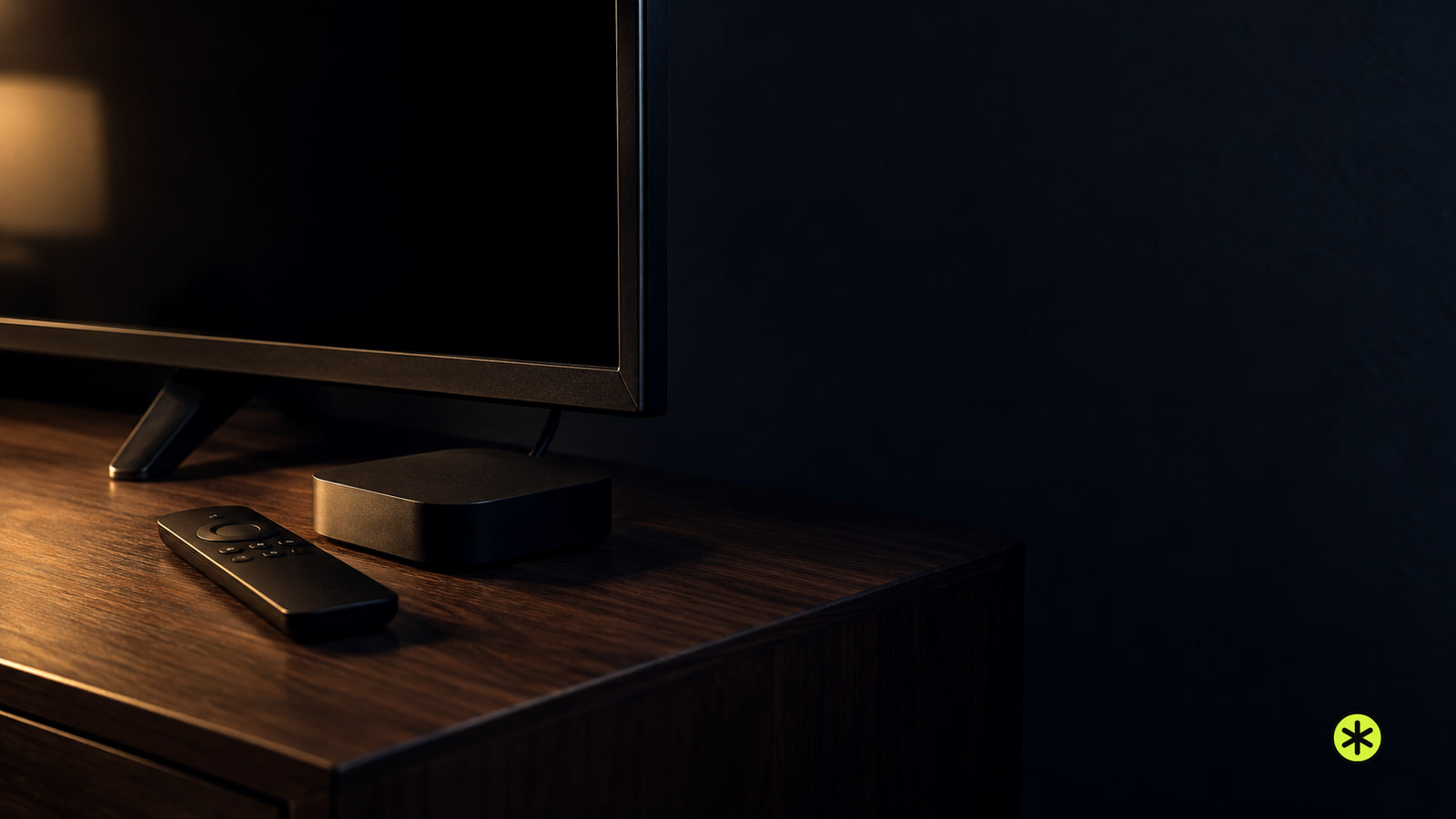 Corner of a dark television on a walnut sideboard with a small black streaming box and a slim remote in front, lit low by a warm lamp at night.