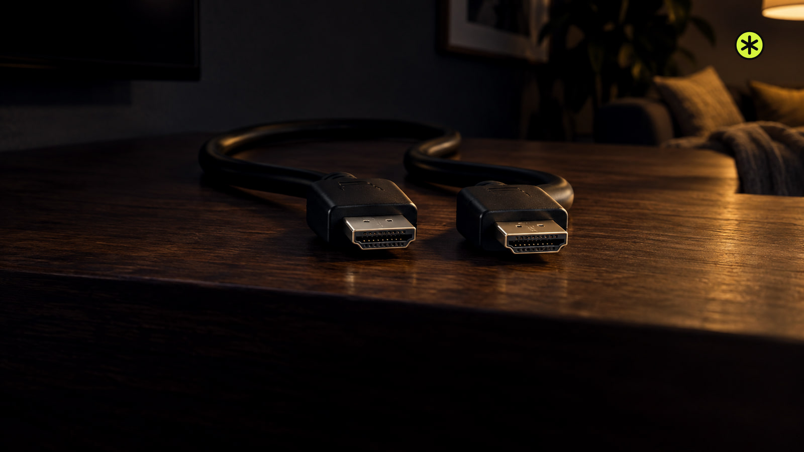 Two black HDMI plug ends with metal tips lie side by side on a walnut sideboard at night, lit low from the right by a warm lamp.