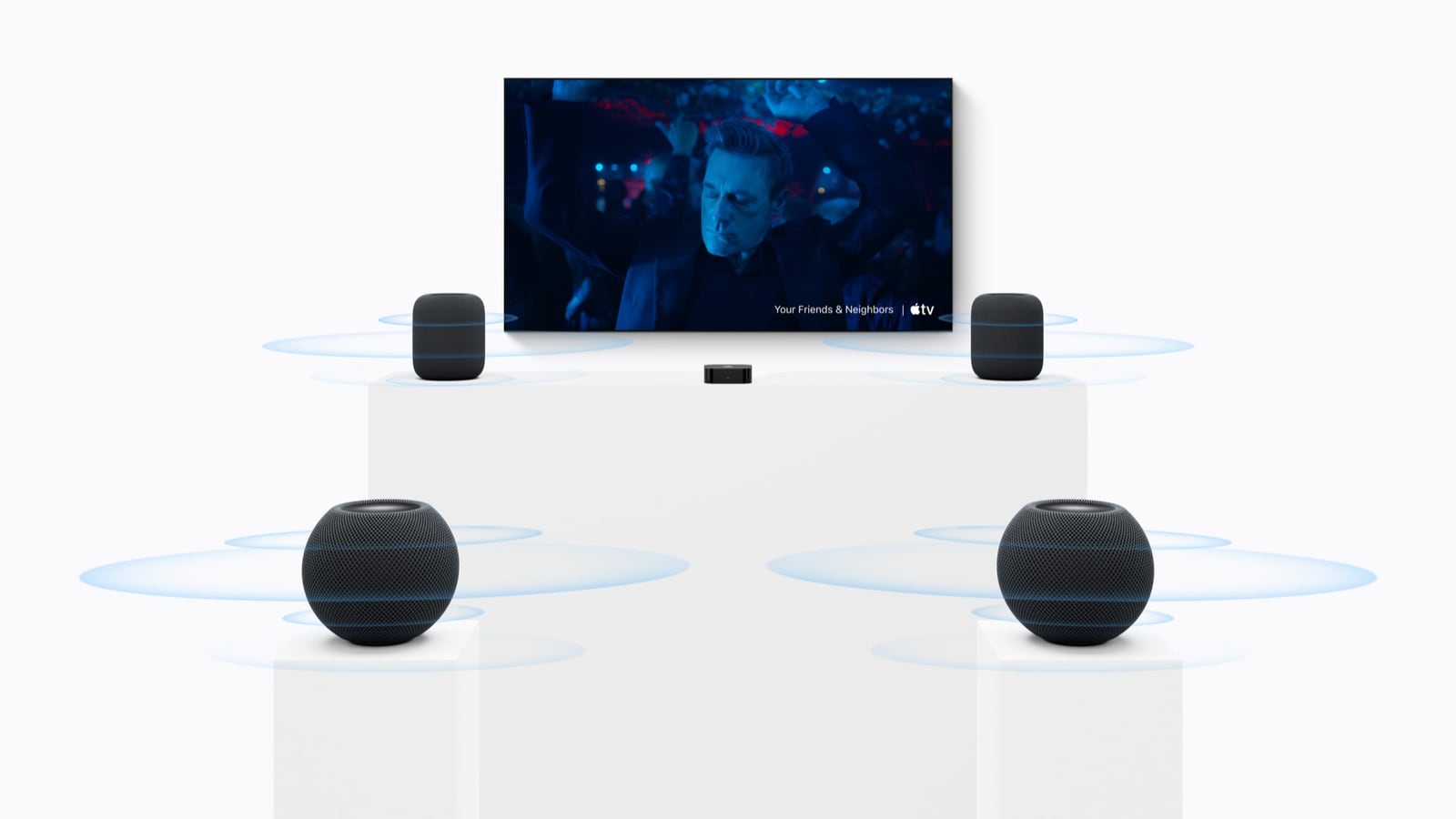 Two taller HomePods flank a television, with two HomePod minis behind them and blue rings around all four speakers.