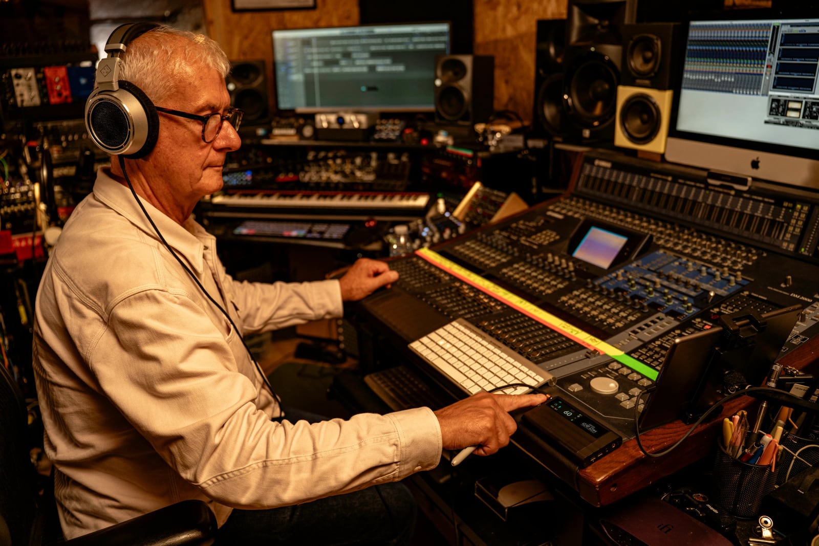 A man wearing headphones operates an iFi DAC and headphone amplifier beside a studio mixing console.