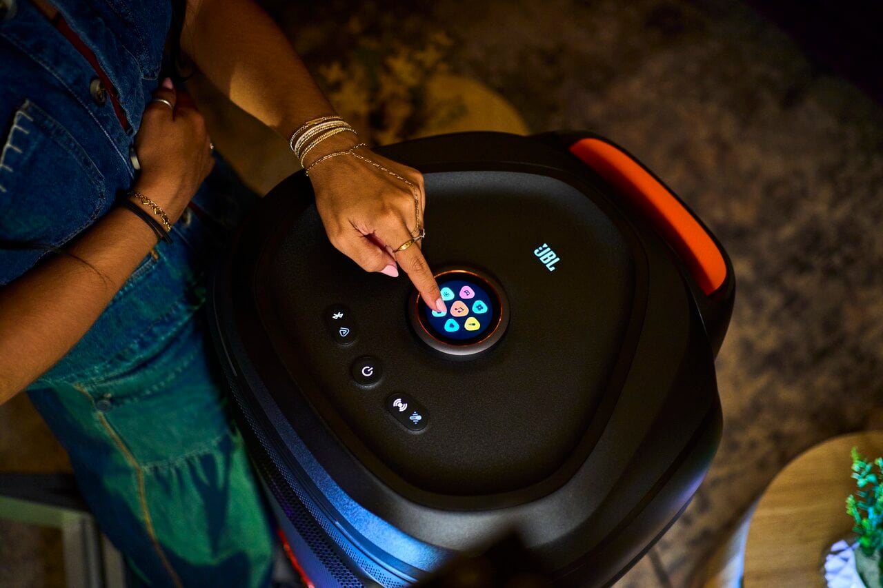 A person operates the circular touchscreen on top of a JBL party speaker.