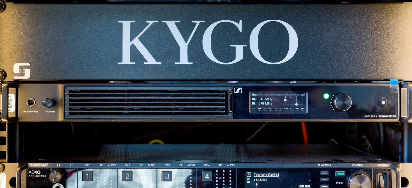 A Sennheiser Spectera base station sits in a rack beneath a panel marked KYGO.