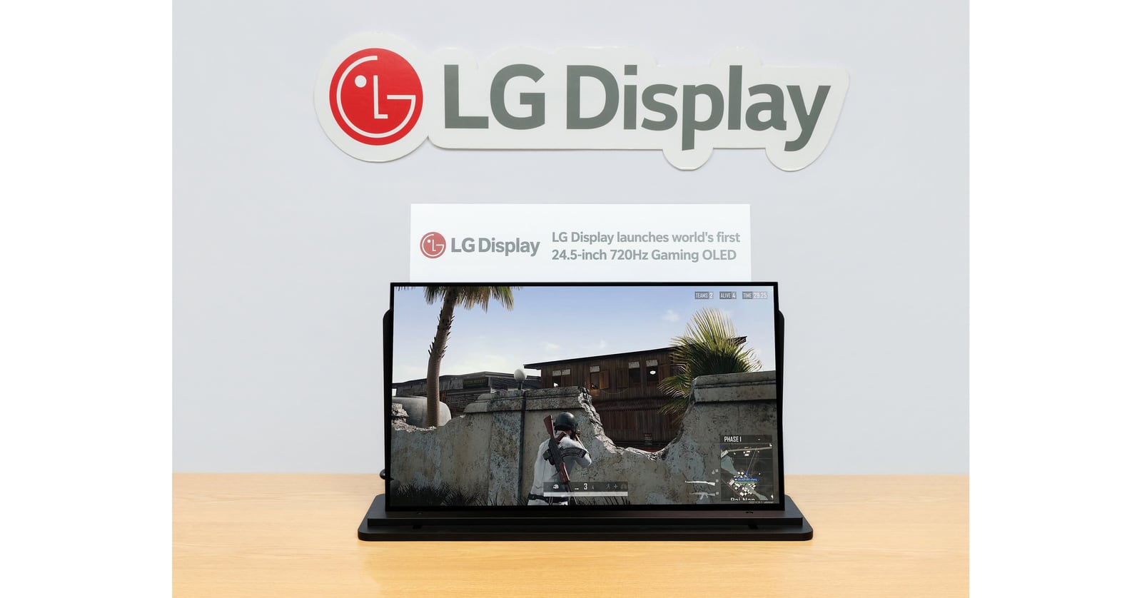 A gaming display shows a shooter game on a wooden table beneath LG Display branding and 24.5-inch 720Hz OLED signage.