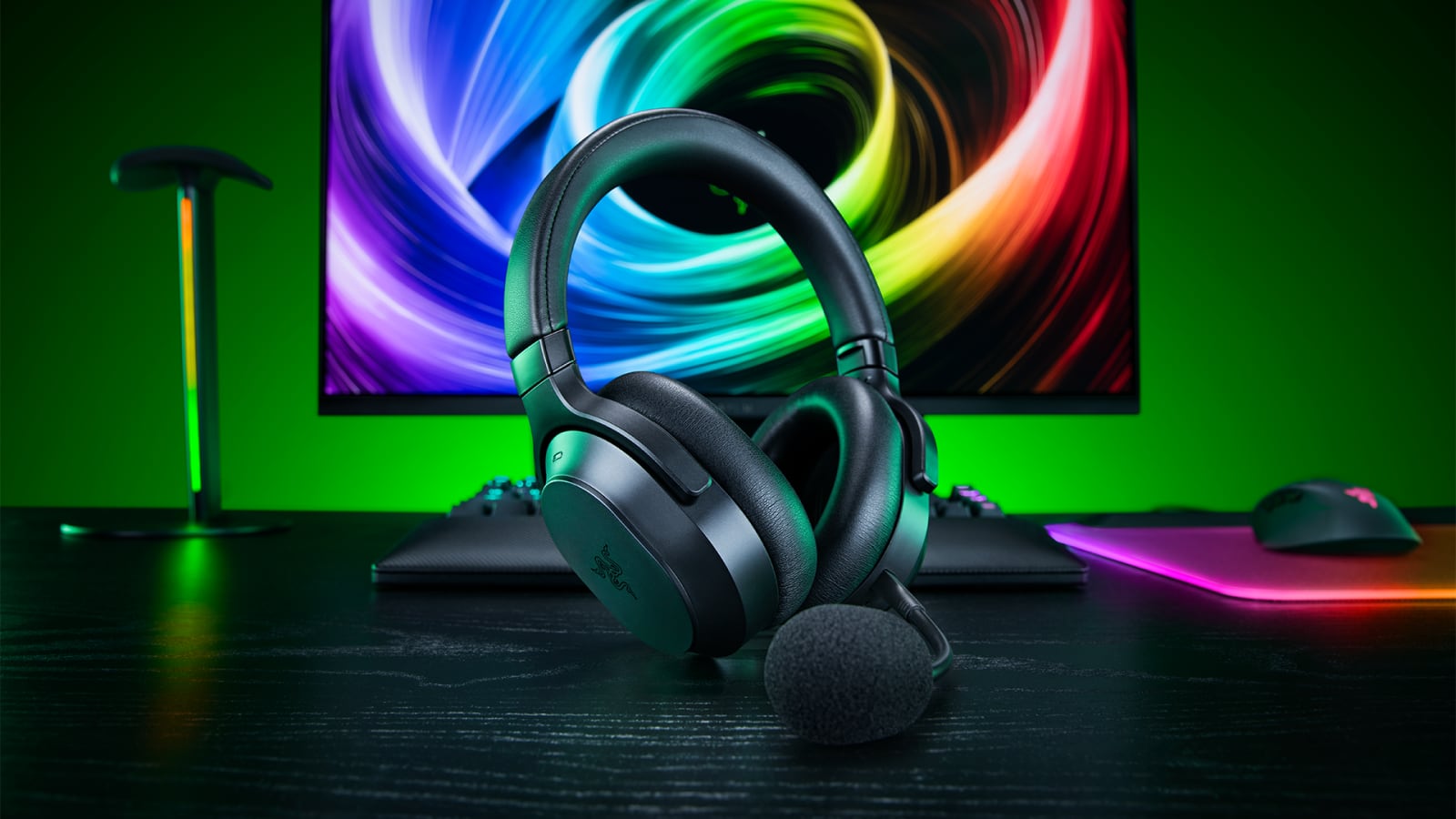 Black Razer headset with a boom microphone on a desk in front of a colorful monitor.