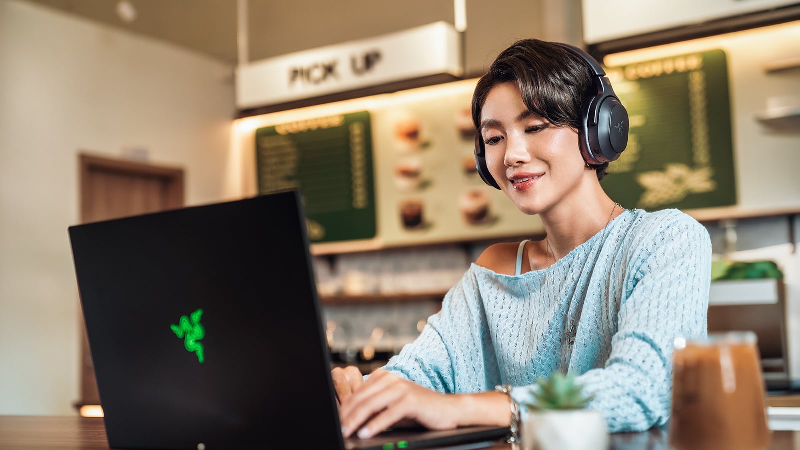 A person wearing a black Razer headset while using a laptop at a café table.