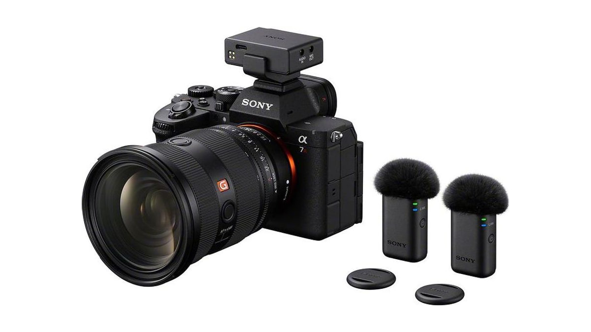 Sony camera with a wireless receiver mounted on top, beside two microphone transmitters with furry windscreens.