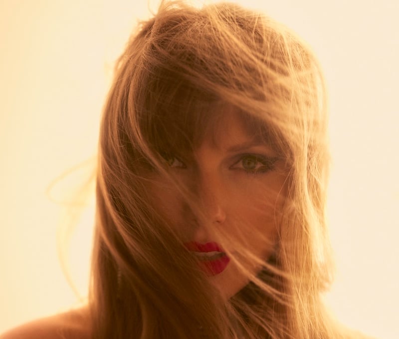 A warmly lit portrait with windblown hair across the face and red lipstick.