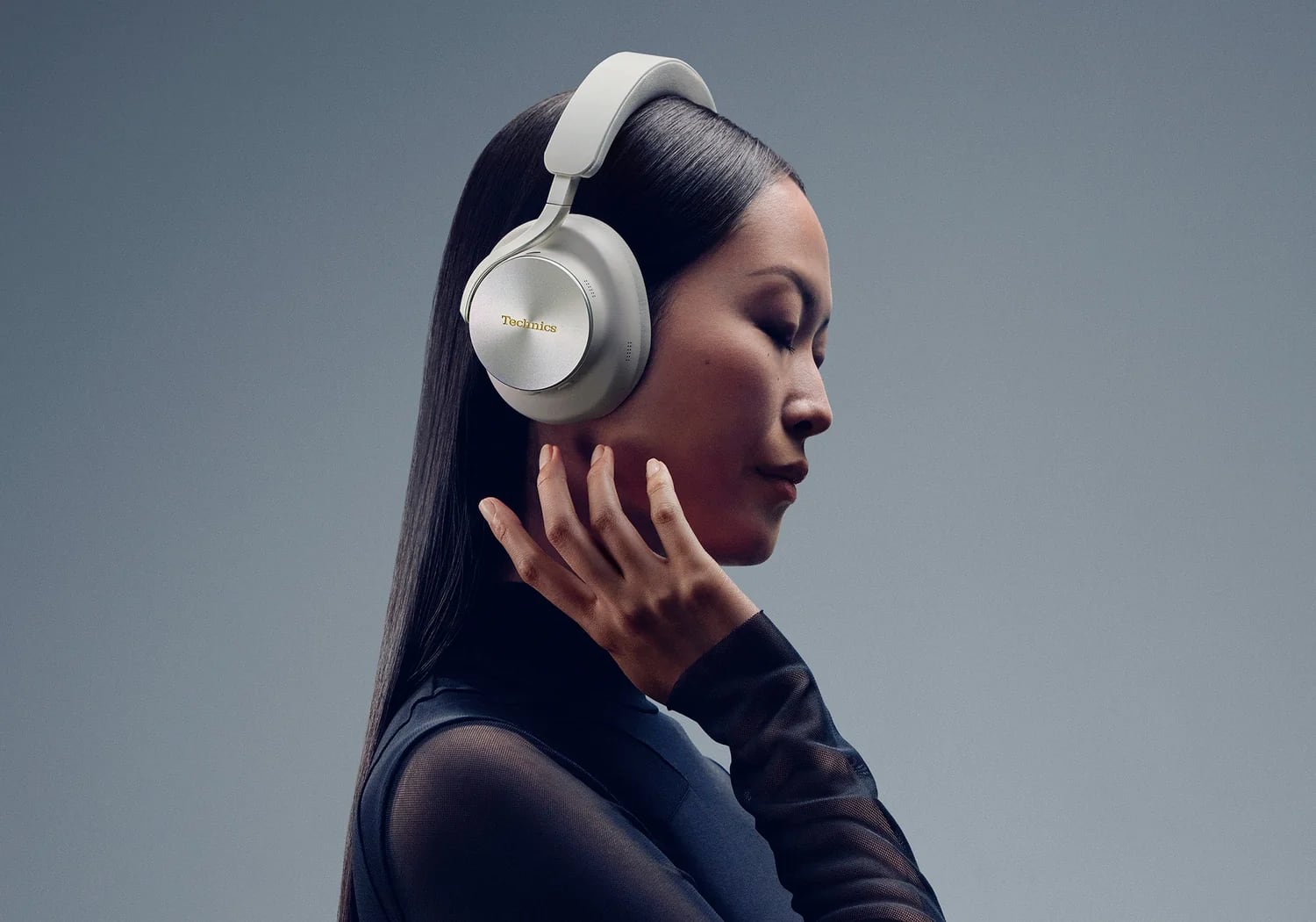 A woman wearing light gray Technics over-ear headphones with a metallic ear cup and padded headband.