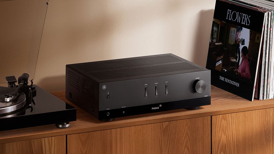 A black Yamaha stereo receiver sits on a wooden cabinet beside a turntable and vinyl records.